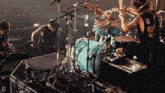 a man in a black tank top with the letter o on it is playing drums