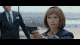 a woman holding a gun in front of a man in a suit and tie