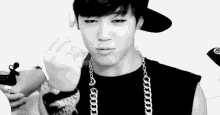 a black and white photo of a young man wearing a hat and necklace .