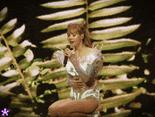 a woman is singing into a microphone on a stage with leaves in the background