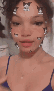 a woman wearing a blue tank top and a necklace is taking a selfie with a face mask on her face .