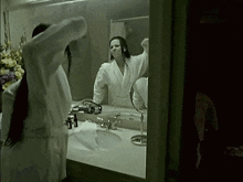a woman in a bathrobe looks at herself in a mirror