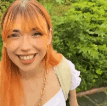 a close up of a woman with red hair smiling in front of a tree .