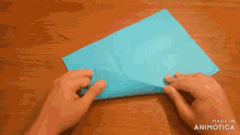 a person is folding a piece of blue paper on a table .