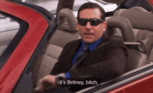 a man in a suit and tie is sitting in a red car and says it 's britney bitch