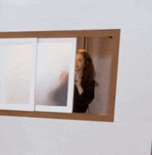 a woman is standing in front of a window and looking out