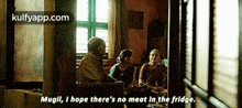 a group of people are sitting around a table in a dark room and one of them is talking about meat in the fridge .