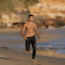 a shirtless man is running on the beach holding a water bottle