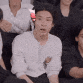 a man in a white shirt is sitting in a group of people and making a funny face .