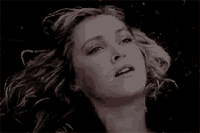 a close up of a woman 's face with a black background and her hair blowing in the wind .