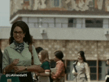 a woman wearing glasses and a scarf is smiling in front of a building that has the number 10 on it