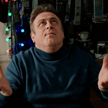 a man in a blue turtleneck sweater is looking up with his hands in the air