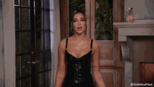 a woman in a black leather dress is standing in front of a fireplace in a living room .