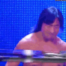 a shirtless wrestler is standing in front of a blue background .