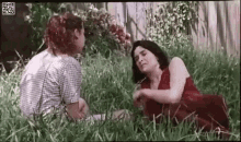 two women are sitting in the grass looking at each other .