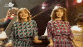 two women are dancing in front of a piano and the words click & classics are on the bottom of the screen