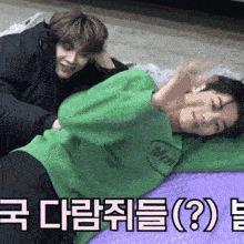 two young men are laying on a bed and one of them is wearing a green shirt with mm on it .