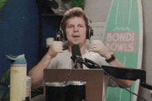 a man wearing headphones is holding a cup in front of a sign for bondi bowls