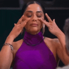 a woman in a purple halter top is touching her face with her hands .