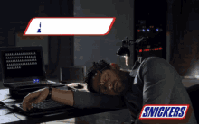 a man is sleeping in front of a laptop with a snickers logo behind him