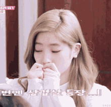 a girl with blonde hair is covering her mouth with her hands in front of a foreign language advertisement