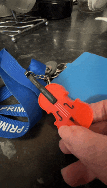 a person is holding a violin keychain in front of a blue lanyard that says prima