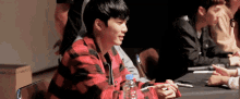 a man in a plaid shirt is sitting at a table with a bottle of water in his hand .