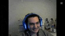 a man wearing blue headphones is smiling while sitting in front of a table filled with bottles of alcohol .