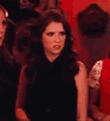 a woman in a black dress is sitting in a row of people .