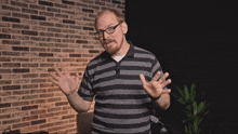 a man wearing glasses and a striped shirt is waving his hands