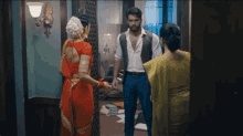 a man and a woman are standing next to each other in a room . the woman is wearing a red sari .