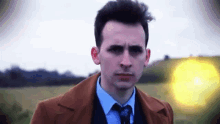 a man in a suit and tie is standing in a field with a yellow light in the background .