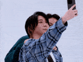 a man in a plaid shirt is taking a selfie with another man in a green sweater