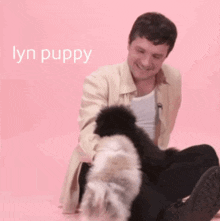 a man is playing with a small black and white dog on a pink background with lyn puppy written on the bottom
