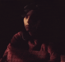 a woman in a red shirt is looking at the camera in the dark