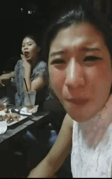 a woman is crying while sitting at a table with a plate of food