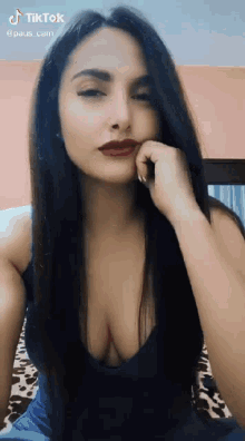 a woman with long black hair and red lipstick is sitting on a bed with her hand on her chin .