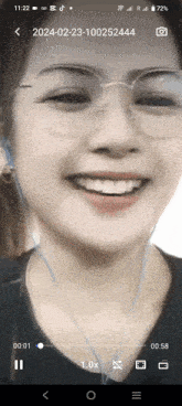 a phone screen shows a woman wearing glasses and ear buds