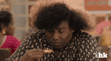 a man with curly hair is eating a piece of food with xhk written on the bottom