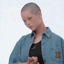 a woman with a shaved head is wearing a denim jacket with a louis vuitton patch on the pocket
