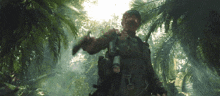 a soldier is walking through a lush green forest holding a gun .