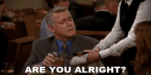 a man in a suit and tie is being served by a waiter and says " are you alright " at the bottom