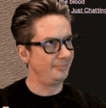 a man wearing glasses and a black shirt is smiling and looking to the side .