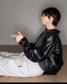 a person wearing a black leather jacket and white pants is laying on the floor pointing