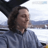a man in a blue shirt is sitting in a car drinking orange juice ..