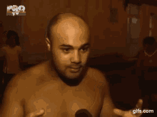a man without a shirt is flexing his muscles in front of a microphone .