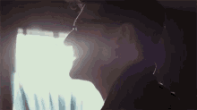 a man wearing glasses is smiling in front of a window in a dark room .