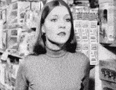 a woman in a turtleneck stands in front of a shelf with a sign that says ' johnson '