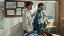 two young men are standing next to each other in front of a bulletin board