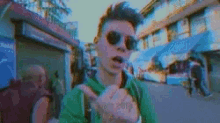 a man wearing sunglasses and a green shirt is giving the middle finger while walking down a street .